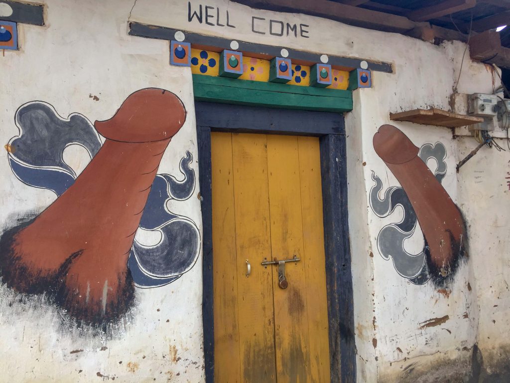 Sacred phallus art of Bhutan decorating the walls either side of a yellow door.
