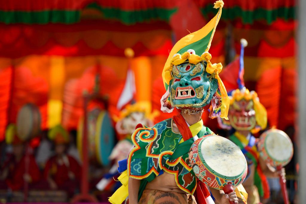 A monks performing a ritual cham dance wearing elaborate and colourful robes and masks.