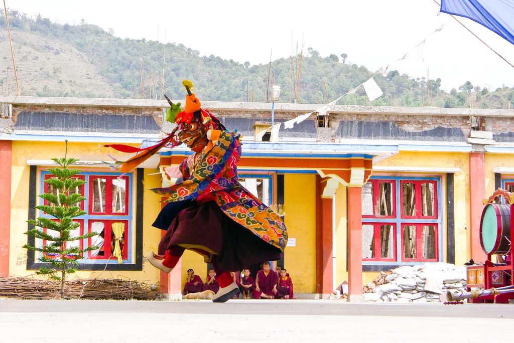 A monk swirl his robes of red, blue, green and gold as they perform a ritual Cham Dance against a mountain backdrop.