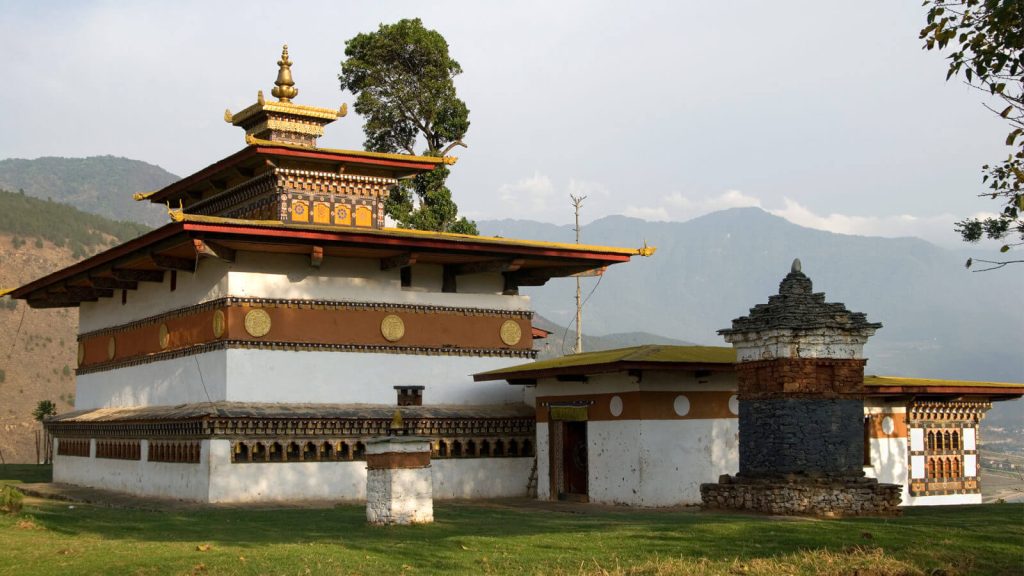 Chimi Lhakhang (Bhutan's Fertility Temple) shining in the sunlight against a backdrop of mountains.