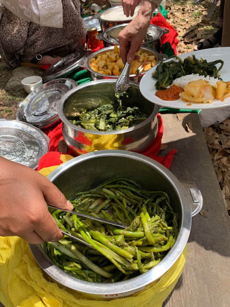Picnic by the Paro river in Bhutan. Students on the Bhutan Yoga adventure fill their plates with colourful vegetables, rice and sauces.