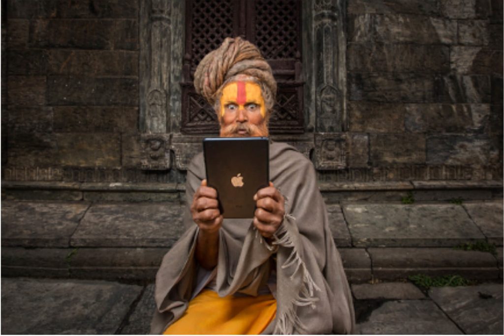 Ancient and modern worlds collide in this sadhu’s life. A sadhu sits looking at an Apple I-pad. Pashupati, Nepal.
